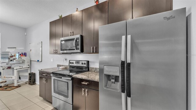 428 Aragosa Dr, Davenport, FL 33837 - kitchen with stainless steel appliances, dark brown cabinets, light tile patterned floors, baseboards, and a textured ceiling