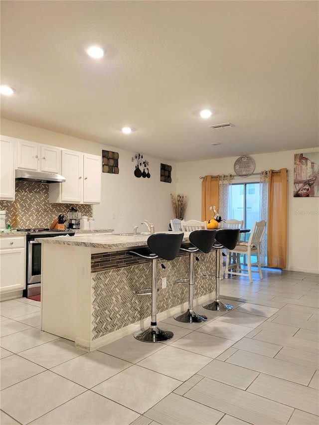 1378 Fox Squirrel Dr, Davenport, FL 33897 - kitchen with stainless steel range with electric cooktop, under cabinet range hood, backsplash, white cabinetry, and recessed lighting