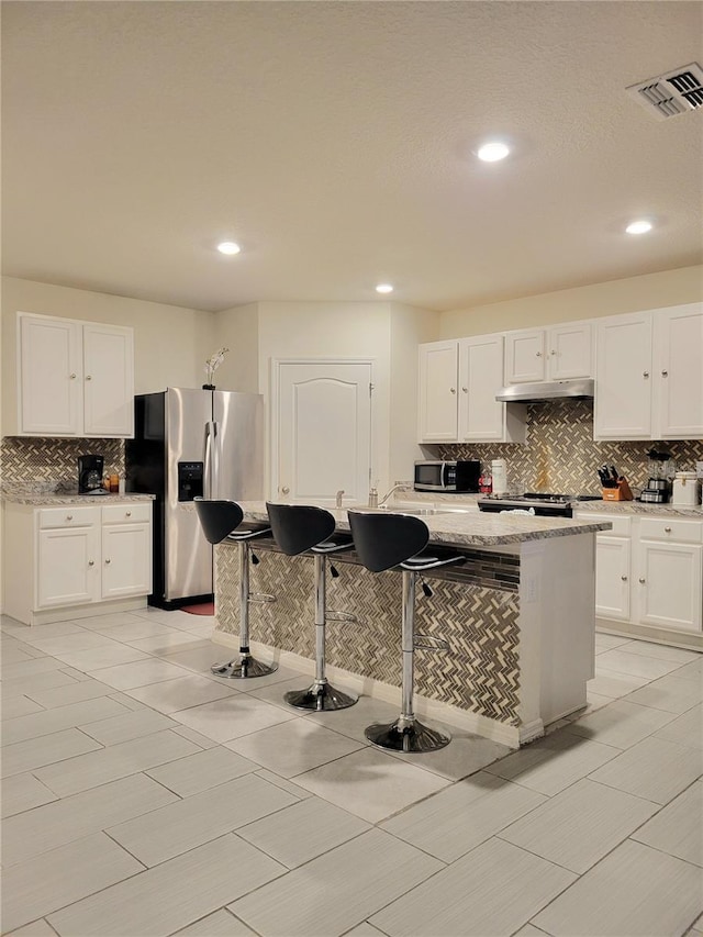 1378 Fox Squirrel Dr, Davenport, FL 33897 - kitchen featuring stainless steel appliances, tasteful backsplash, under cabinet range hood, white cabinets, and light stone counters