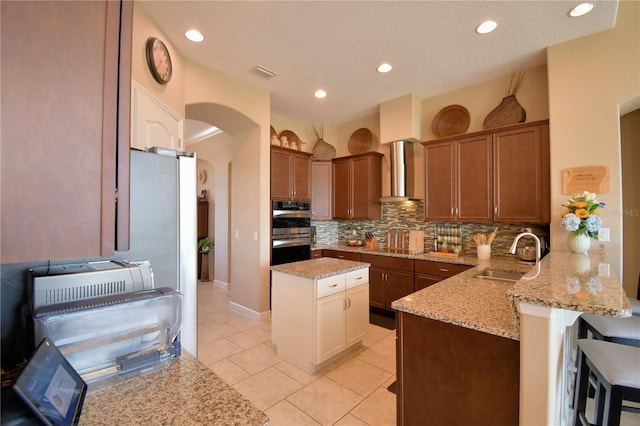 2340 Pinehurst Ct, Davenport, FL 33837 - kitchen featuring wall chimney range hood, arched walkways, a peninsula, double oven, and backsplash