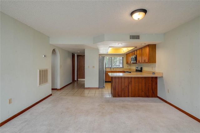 5102 Village Ct Unit E-2, Lake Wales, FL 33898 - kitchen featuring appliances with stainless steel finishes, brown cabinets, light carpet, a peninsula, and baseboards