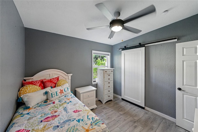1140 W Seminole Trl, Bartow, FL 33830 - bedroom featuring a barn door, a textured wall, light wood-style floors, baseboards, and a ceiling fan