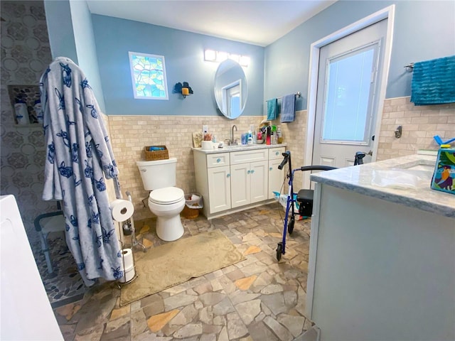 2213 W Pilaklakaha Ave, Auburndale, FL 33823 - bathroom featuring vanity, tile walls, a wainscoted wall, stone finish floors, and toilet
