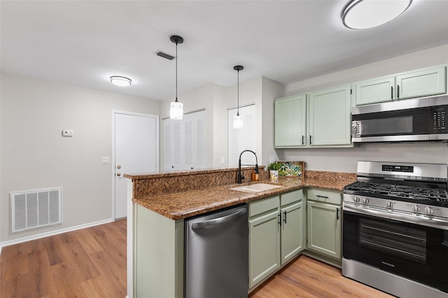 703 Magnolia Pl Unit 703, Winter Haven, FL 33884 - kitchen with appliances with stainless steel finishes, a sink, green cabinets, a peninsula, and light wood-style flooring