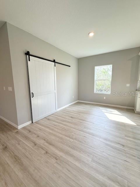 4956 San Lorenzo Dr, Sebring, FL 33872 - unfurnished bedroom featuring baseboards, a barn door, and light wood-type flooring