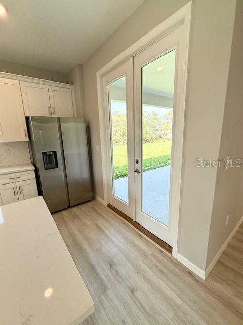 4956 San Lorenzo Dr, Sebring, FL 33872 - kitchen with stainless steel fridge, white cabinetry, light wood finished floors, and light countertops