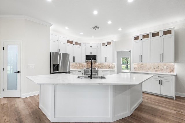 5820 E Johnson Ave, Haines City, FL 33844 - kitchen featuring appliances with stainless steel finishes, a large island with sink, light wood-style flooring, white cabinets, and crown molding