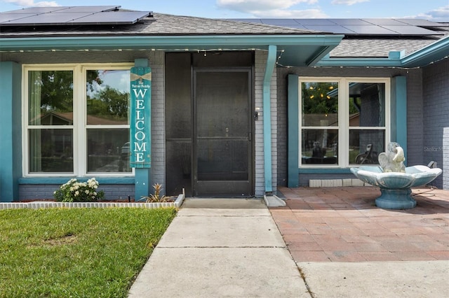 704 Butternut Pl, Lakeland, FL 33813 - view of exterior entry featuring brick siding, solar panels, and roof with shingles