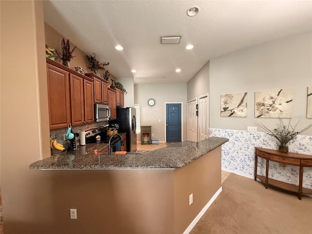 13443 Graham Yarden Dr, Riverview, FL 33579 - kitchen with appliances with stainless steel finishes, dark stone countertops, light colored carpet, a peninsula, and brown cabinetry