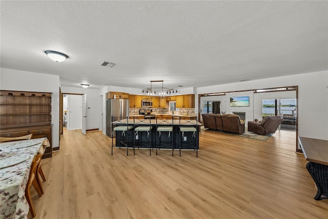914 Mangham Rd, Babson Park, FL 33827 - kitchen with appliances with stainless steel finishes, brown cabinetry, light wood-style floors, tasteful backsplash, and a textured ceiling