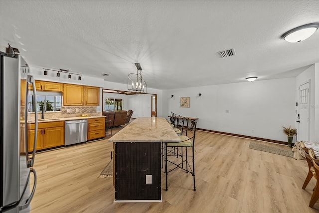 914 Mangham Rd, Babson Park, FL 33827 - kitchen featuring appliances with stainless steel finishes, a breakfast bar, light wood-style flooring, a textured ceiling, and tasteful backsplash