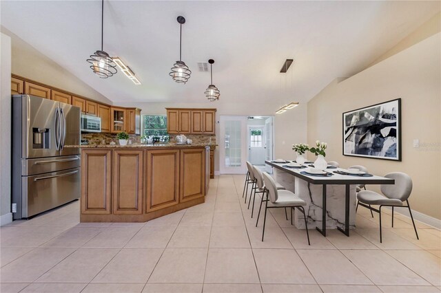 1823 N Olivia Dr, Avon Park, FL 33825 - kitchen with stainless steel appliances, vaulted ceiling, brown cabinets, light tile patterned flooring, and a kitchen island