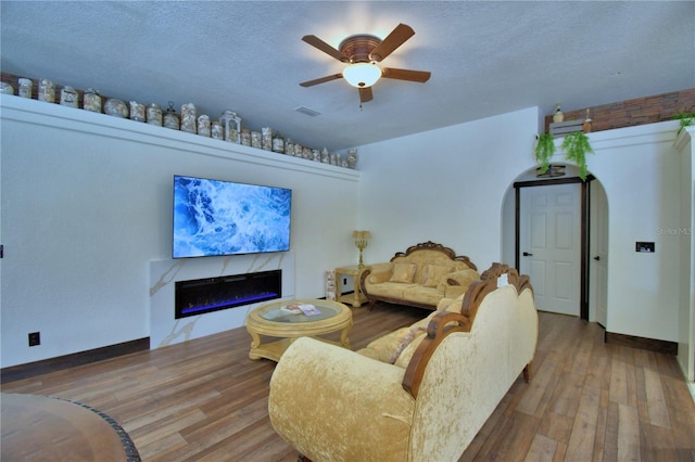 10708 Belo Horizonte Ave, Clermont, FL 34711 - living area featuring a glass covered fireplace, ceiling fan, wood finished floors, arched walkways, and a textured ceiling