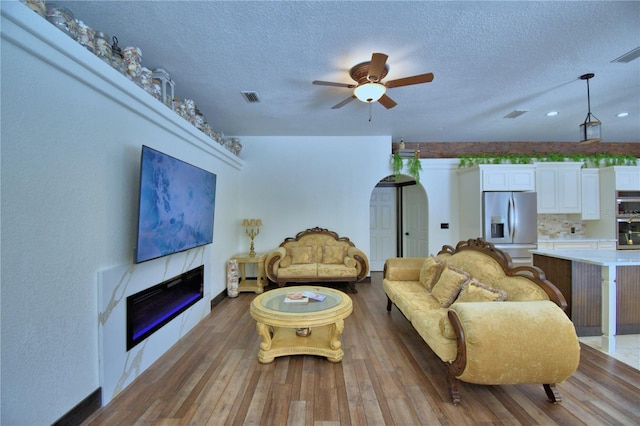 10708 Belo Horizonte Ave, Clermont, FL 34711 - living room featuring a textured ceiling, a ceiling fan, hardwood / wood-style floors, a glass covered fireplace, and arched walkways