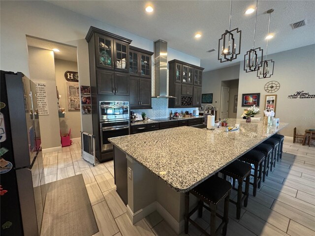 25863 Crossings Bluff Ln, Sorrento, FL 32776 - kitchen with wall chimney exhaust hood, stainless steel appliances, a breakfast bar, light stone counters, and a large island with sink