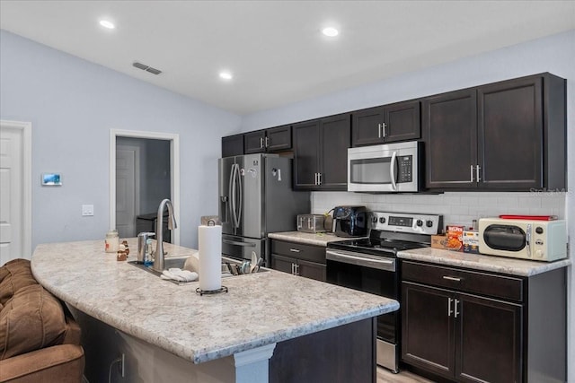 910 Blue Tide Ln, Lakeland, FL 33809 - kitchen with stainless steel appliances, tasteful backsplash, light countertops, vaulted ceiling, and an island with sink
