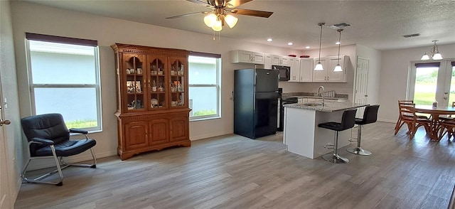 1736 3rd St NE, Winter Haven, FL 33881 - kitchen with black appliances, a kitchen bar, light wood-type flooring, ceiling fan, and hanging light fixtures