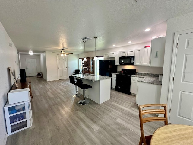 1736 3rd St NE, Winter Haven, FL 33881 - kitchen featuring black appliances, a textured ceiling, light wood-style floors, a breakfast bar area, and white cabinetry