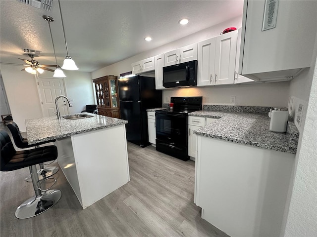 1736 3rd St NE, Winter Haven, FL 33881 - kitchen with black appliances, light wood finished floors, a breakfast bar, white cabinetry, and pendant lighting