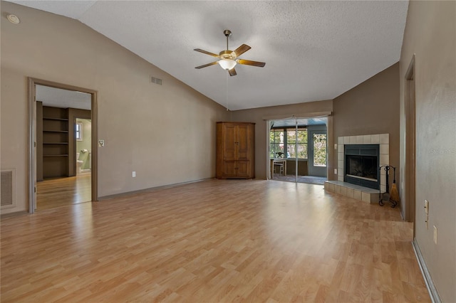 3408 Cove Ct W, Winter Haven, FL 33880 - unfurnished living room featuring lofted ceiling, ceiling fan, light wood-type flooring, a textured ceiling, and a tiled fireplace