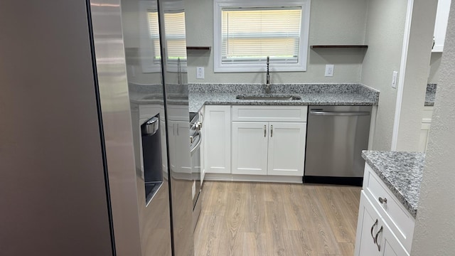 713 4th St NE, Fort Meade, FL 33841 - kitchen featuring stainless steel appliances, light wood-style floors, white cabinetry, light stone counters, and a textured wall