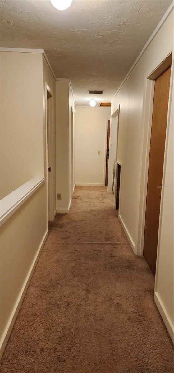 corridor with a textured ceiling, ornamental molding, and carpet floors