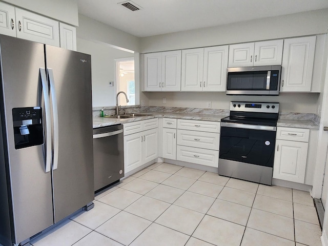 kitchen with appliances with stainless steel finishes, white cabinetry, sink, and light tile flooring