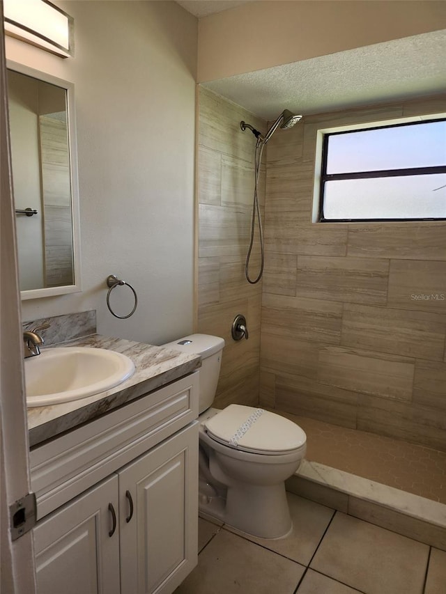 bathroom featuring toilet, a tile shower, tile flooring, a textured ceiling, and vanity