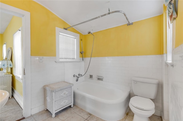 bathroom featuring lofted ceiling, toilet, a wealth of natural light, and tile walls