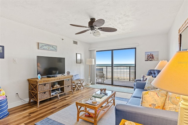 living room featuring a textured ceiling, light hardwood / wood-style floors, ceiling fan, and a water view