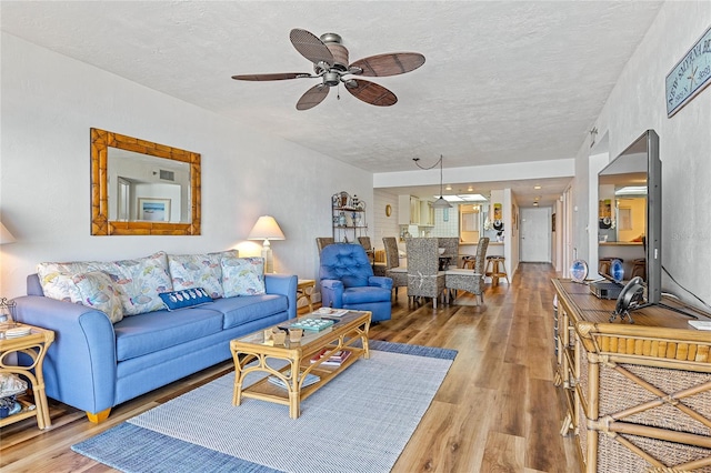 living room with a textured ceiling, ceiling fan, and light hardwood / wood-style flooring