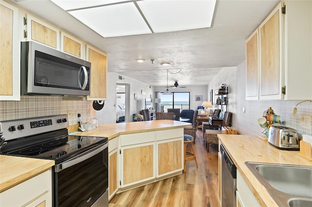 kitchen featuring backsplash, light hardwood / wood-style floors, stainless steel appliances, and kitchen peninsula