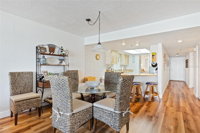 dining area with a skylight, light hardwood / wood-style flooring, and a textured ceiling
