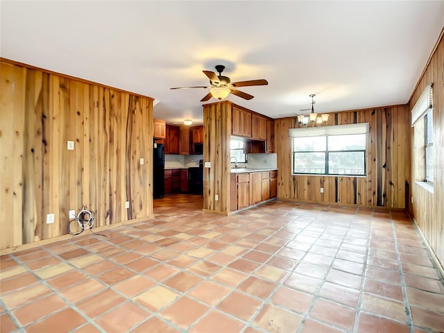 unfurnished living room featuring light tile flooring, wood walls, sink, and ceiling fan with notable chandelier