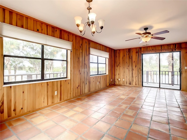 tiled spare room featuring wood walls and ceiling fan with notable chandelier