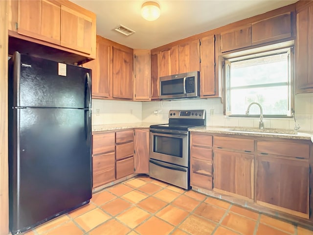 kitchen with light tile floors, appliances with stainless steel finishes, light stone counters, and sink