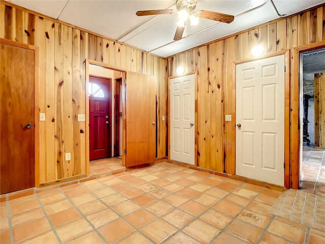 tiled empty room featuring wood walls and ceiling fan