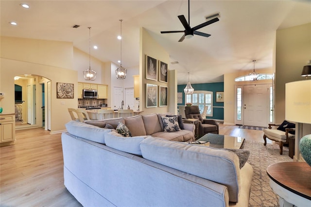 living room with light hardwood / wood-style floors, high vaulted ceiling, and ceiling fan with notable chandelier