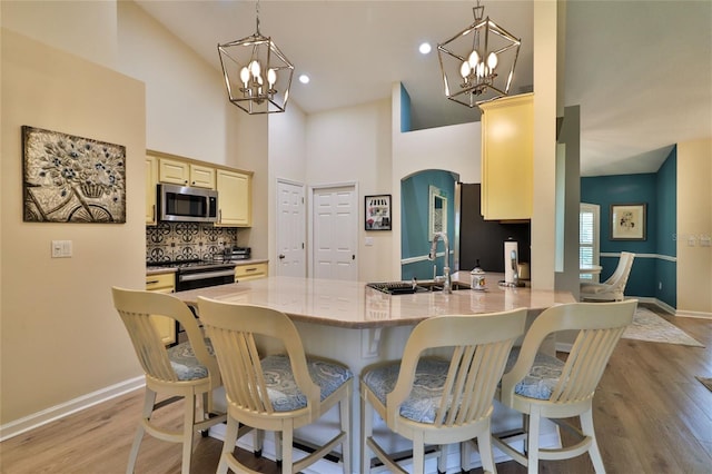 dining space featuring high vaulted ceiling, sink, a chandelier, and light hardwood / wood-style flooring