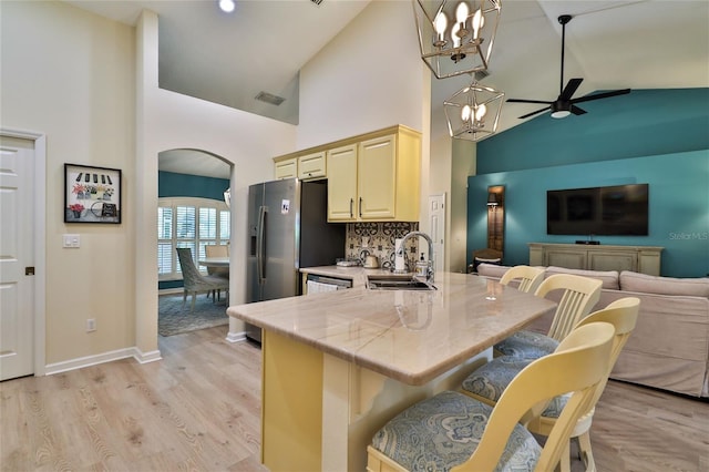 kitchen featuring sink, light hardwood / wood-style flooring, a breakfast bar area, high vaulted ceiling, and ceiling fan with notable chandelier