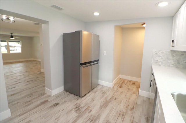 kitchen featuring ceiling fan, tasteful backsplash, white cabinetry, light wood-type flooring, and sink