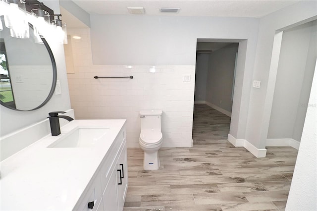 bathroom with toilet, large vanity, hardwood / wood-style floors, and tile walls