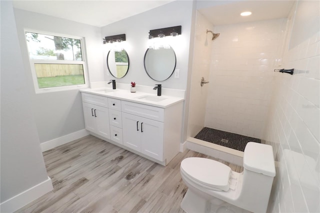 bathroom with hardwood / wood-style floors, tiled shower, toilet, and dual bowl vanity