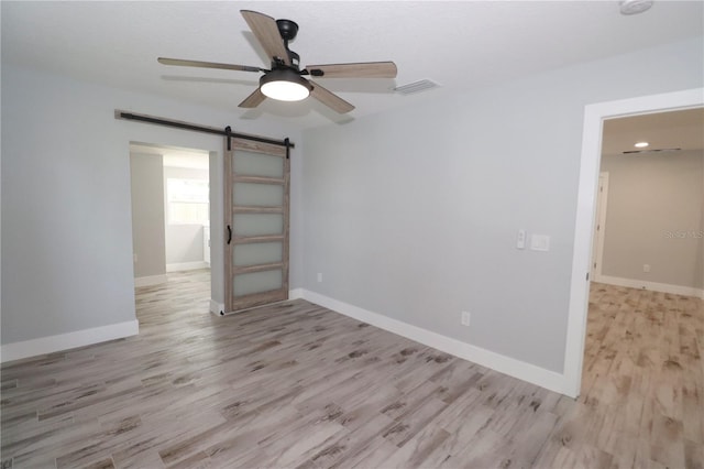 spare room with a barn door, ceiling fan, and light wood-type flooring