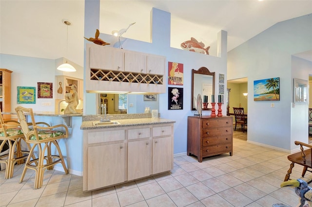 kitchen featuring light brown cabinets, light tile floors, decorative light fixtures, and light stone counters