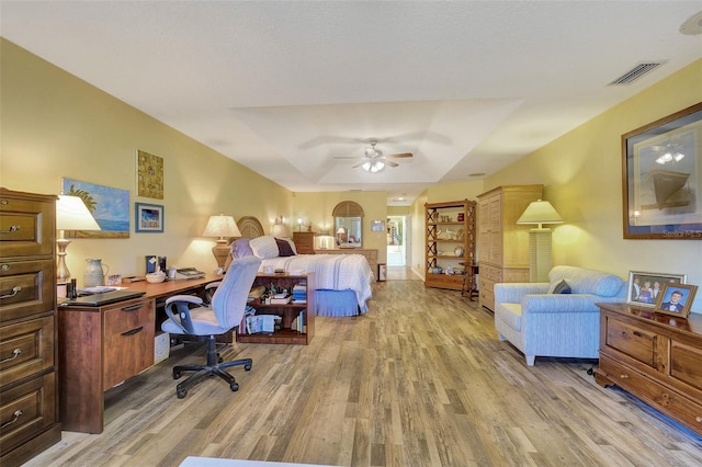 office featuring a tray ceiling, ceiling fan, and light wood-type flooring