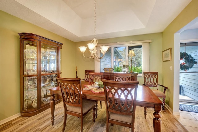 tiled dining area featuring a chandelier and a tray ceiling