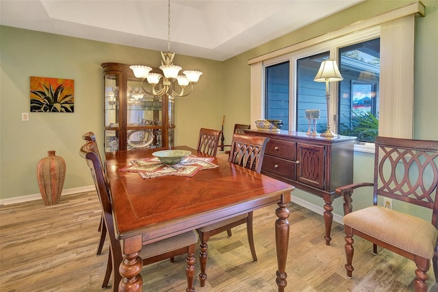 dining space featuring light hardwood / wood-style flooring, a tray ceiling, and a notable chandelier