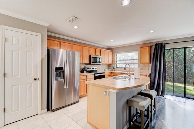 kitchen featuring an island with sink, sink, crown molding, stainless steel appliances, and tasteful backsplash