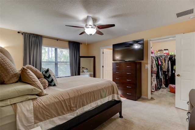 bedroom with a closet, ceiling fan, a textured ceiling, a spacious closet, and light colored carpet